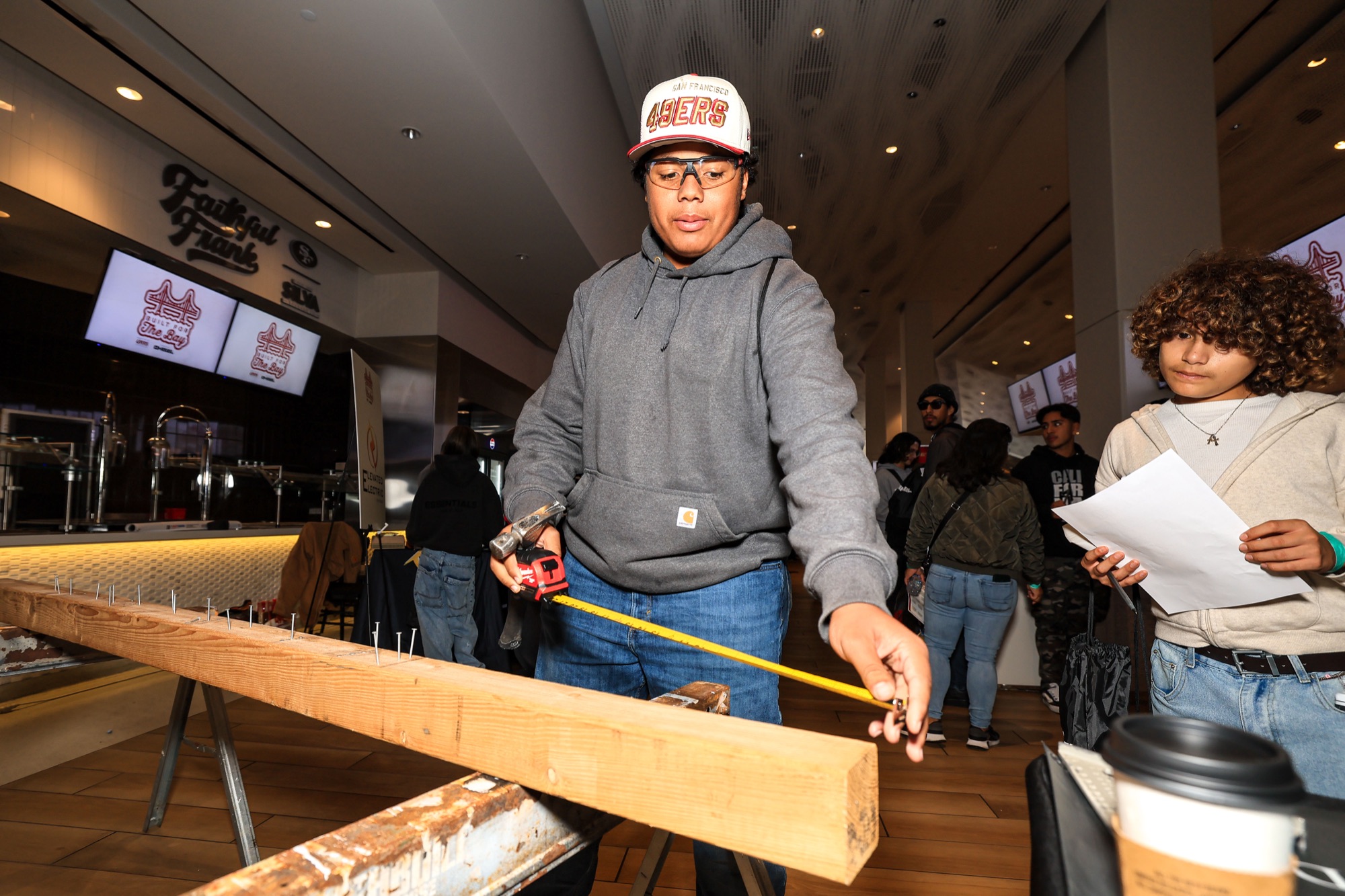 A student measures a length of lumber on sawhorses